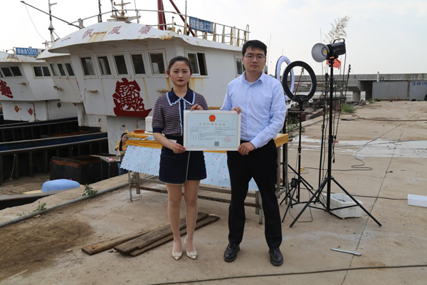 海鮮電商張夢琴與幫辦員手持食品經(jīng)營許可證合影。贛榆區(qū)委宣傳部供圖